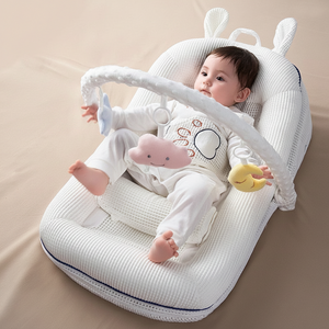 Baby lying in a white baby bouncer with toys on a beige surface