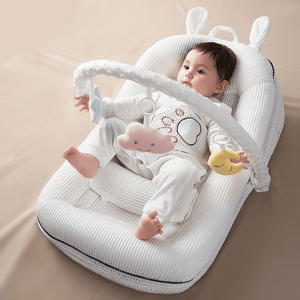 Baby lying in a white baby bouncer with toys on a beige surface