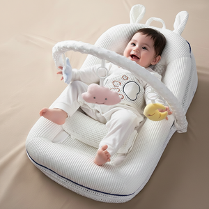 Baby sitting in a white baby bouncer with toys on a beige blanket