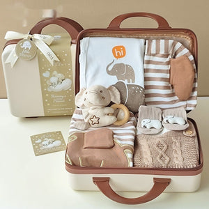 Baby gift set in a suitcase with clothes, toys, and a plush elephant on a beige background