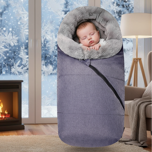 Baby sleeping in a gray and purple swaddle blanket with a snowy window and fireplace in the background.