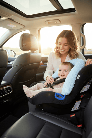 Woman adjusting a baby in a car seat inside a vehicle with a scenic background