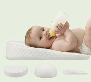 An infant lying on a white DreamLift Anti-Reflux Infant Wedge Pillow while drinking from a bottle.
