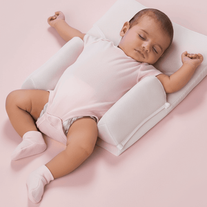 Baby sleeping on a pink blanket with a white wedge pillow