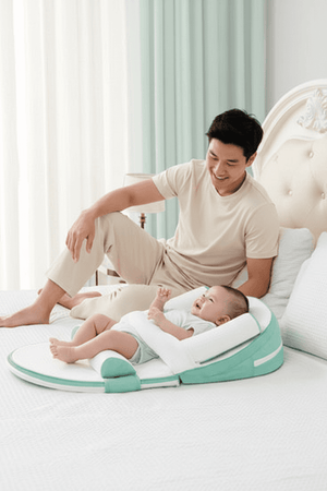 Man sitting on a bed with a baby using a green and white baby support product.