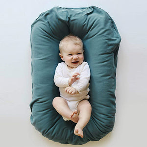 Baby lying on a teal cushion with a plain background