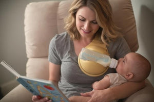 Woman holding a baby and a bottle, reading a book in a cozy setting