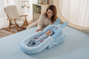 Baby sleeping in a blue bunny-shaped crib on a bed.