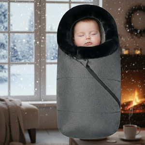 Baby sleeping in a gray swaddle with a black hood in a cozy room with a snowy window view.