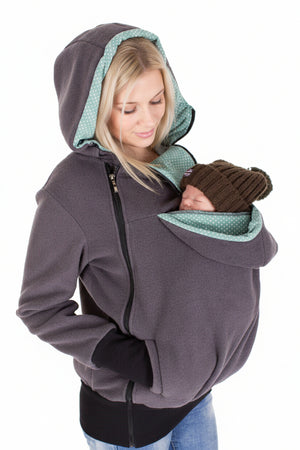 Woman wearing a gray hoodie with green lining, holding a baby in a sling.
