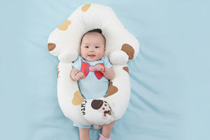 Baby lying on a white dog-shaped cushion with brown spots on a light gray background