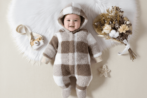 Baby in a checkered onesie lying on a white surface with decorative items around.
