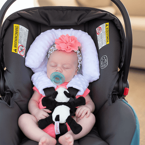 Baby in a car seat with a pacifier and toy, wearing a floral headband.