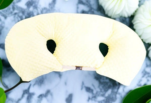 Cream-colored eye mask on a marble surface with green leaves