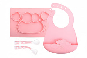 Pink silicone baby plate, bib, spoon, and fork set on a white background