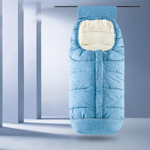 A light blue padded baby sleeping bag with a subtle dotted pattern and a cream-colored inner lining, shown hanging against a minimalist gray studio background.
