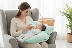 Woman sitting in a chair with a baby on a green cushion, holding a bottle.