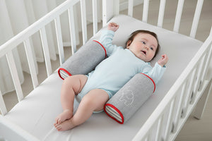 A newborn baby lying on a gray anti-roll safety support pillow with red trim.