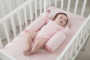 Baby lying on a pink crib bumper pad in a white crib.