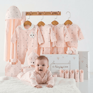 Baby in pink outfit with baby clothes and new born gift set in the background
