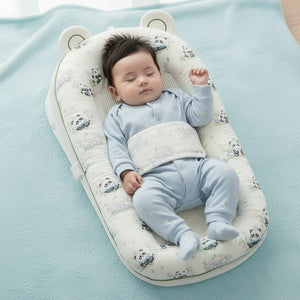 A soft baby bassinet or diaper bag with a white fabric exterior printed with cute black-and-white panda faces and small pastel floral details, shown on a beige bed. The product has padded sides, a mesh front panel, a padded belly pad, and small bear ears on the top.