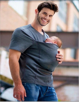 Man holding a baby in a sling outdoors