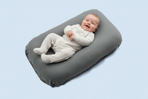 Baby lying on a gray cushion against a light blue background