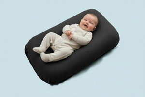 Baby lying on a gray cushion against a light blue background