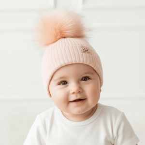 Baby wearing a pink knit hat with a large pom-pom on a light background