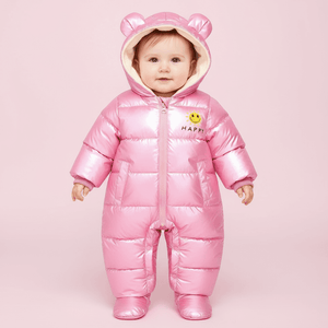 Baby wearing a pink puffer snowsuit with bear ears on a pink background