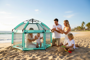 Family with children playing on a beach near a transparent green play tent.