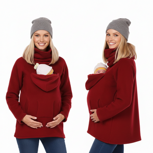Two views of a pregnant woman modeling a deep red fleece maternity sweater with a built-in hooded baby carrier pocket. She is wearing a gray knit beanie and blue jeans, with a baby nestled inside the pocket in one view.