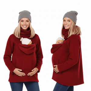 Two views of a pregnant woman modeling a deep red fleece maternity sweater with a built-in hooded baby carrier pocket. She is wearing a gray knit beanie and blue jeans, with a baby nestled inside the pocket in one view.