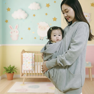 Woman wearing a baby in a gray sling against a plain background