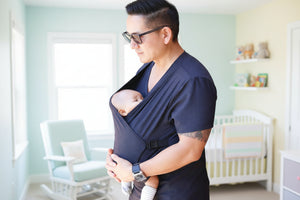 A man wearing a black T-shirt baby carrier with a baby in it.