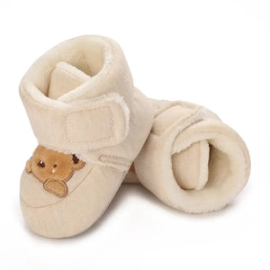 Beige baby booties with a teddy bear design on a white background