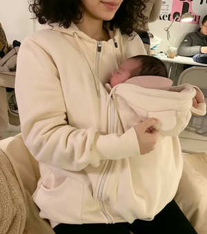 Person holding a baby in a white baby carrier indoors.