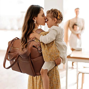 Woman holding a child and a brown leather bag in a bright indoor setting