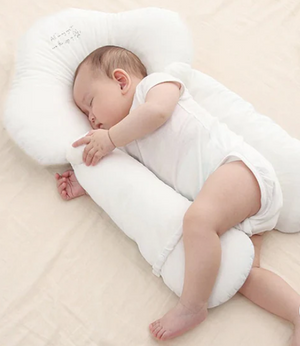 A baby lying on a white, solid patterned sleep pillow designed for infants.