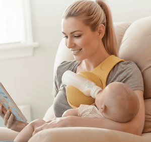 Woman breastfeeding a baby while reading a book on a couch