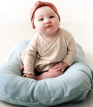 A newborn baby lying in a brown, cushioned baby lounger nest.