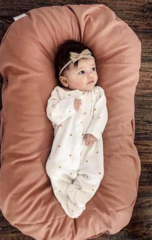 A newborn baby lying in a brown, cushioned baby lounger nest.