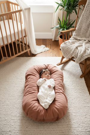 A newborn baby lying in a brown, cushioned baby lounger nest.