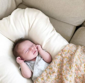 A newborn baby lying in a brown Cosydream Newborn Lounger Baby lounger Nest, which is designed to mimic the snug embrace of the womb.