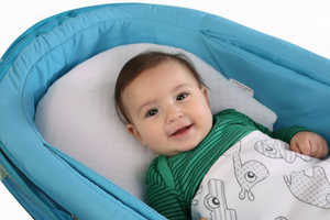 A baby lying on a blue newborn inclined wedge pillow designed to elevate the head and torso, placed in a bassinet.