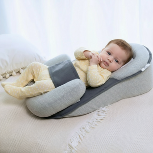 Baby lying on a wedge-shaped baby lounger pillow on the bed