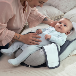 Baby lying on a baby lounger with a woman beside them, both on a soft surface.