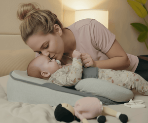 Woman lying on a bed with a baby on a baby lounger pillow