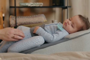 Baby lying on a baby lounger with a pacifier in mouth, surrounded by a cozy room setting.
