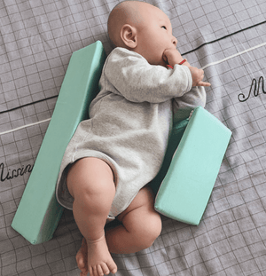 A newborn baby lying on a green Anti-Roll Side Sleeper Pillow Wedge with a removable cover.
